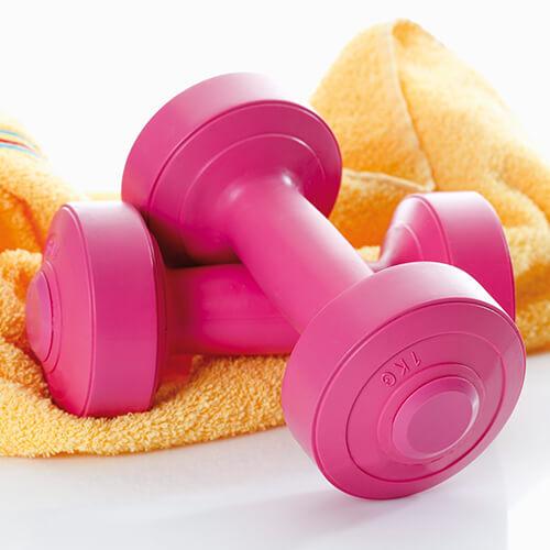 Zwei rosa Hanteln liegen auf einem gelben Handtuch.