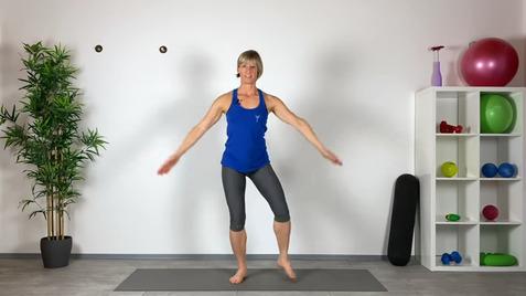 Frau in blauer Sportbekleidung steht barfuß auf einer Yogamatte und führt eine Fitnessübung aus.