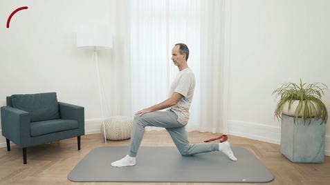 Mann in Sportkleidung macht eine Kniefallübung auf einer Yogamatte in einem hellen Raum.