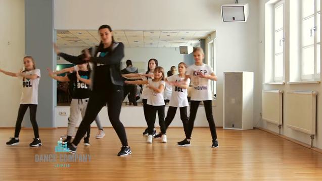 Gruppen von Kindern in Sportkleidung tanzen gemeinsam in einem Spiegellraum unter Anleitung einer Trainerin.