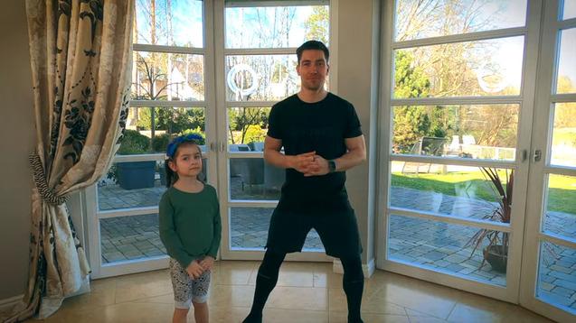 Mann und Mädchen stehen in einem hellen Raum vor großen Fenstern, bereit für ein Workout.