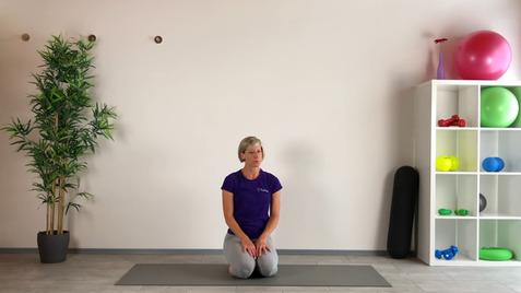 Frau in Sportkleidung kniet auf einer Yogamatte vor einer Wand, Pflanzen und Fitnessgeräten im Hintergrund.