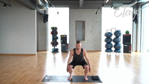 Mann in Sportkleidung führt eine Kniebeuge auf einer Fitnessmatte in einem gut beleuchteten Raum aus.