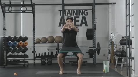 Mann führt eine Fitnessübung in einem Trainingsbereich mit Gewichten und Fitnessgeräten aus.