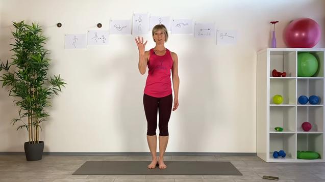 Frau in pinkem Oberteil steht auf einer Yogamatte und hebt mit einer Hand ein Zeichen in die Höhe, im Hintergrund Übungsillustrationen.