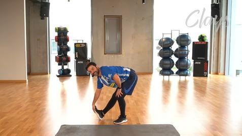 Mann in Sportkleidung dehnt sich in einem Fitnessstudio mit verschiedenen Trainingsgeräten im Hintergrund.