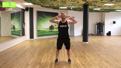 Mann in Sportbekleidung steht in einem Fitnessraum und führt eine Übung mit angehobenen Armen aus.