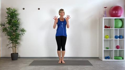 Frau in blauer Sportbekleidung steht barfuß auf einer Sportmatte und zeigt ihre Hände gestikulativ in einem Fitnessraum.