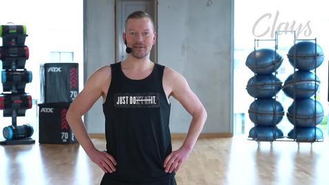 Mann in Sportbekleidung steht in einem Fitnessstudio, im Hintergrund verschiedene Fitnessgeräte und Balancekugeln.