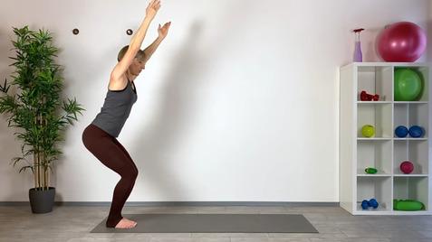 Frau in Sportkleidung macht eine Yoga-Pose auf einer Matte vor einem Regal mit Fitnessgeräten und Pflanzen.