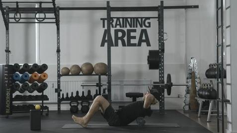 Mann macht eine Übung mit einer Langhantel auf einer Matte in einem modernen Trainingsbereich mit Equipment.