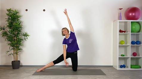 Frau mit kurzem Haar in lila Sportoberteil bei einer Dehnübung auf einer Matte vor einem weißen Hintergrund.