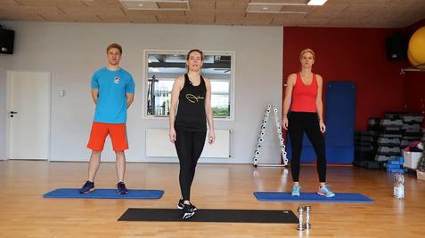 Drei Personen in Sportkleidung stehen auf Teppichmatten in einem Fitnessraum, bereit für ein Workout.
