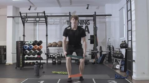 Junger Mann übt mit Widerstandsbändern in einem modernen Fitnessstudio auf einer Trainingsmatte.