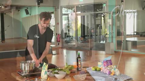 Mann kocht in einer modernen Umgebung, mit Gemüse und Kochutensilien auf einem Tisch in der Nähe.