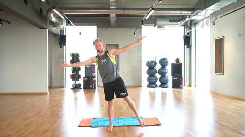Mann in Sportkleidung führt eine Balanceübung auf einer Yogamatte in einem modernen Fitnessraum durch.