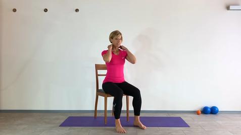 Frau in pinkem Shirt sitzt auf einem Stuhl und zeigt Nackenübungen auf einer Yogamatte.