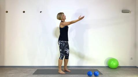 Frau in Sportkleidung steht auf einer Matte und streckt die Arme nach vorn, neben ihr liegen zwei blaue Bälle.