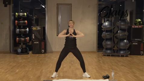 Frau in Sportkleidung führt eine Kniebeuge-Übung in einem Fitnessstudio mit Trainingsgeräten durch.