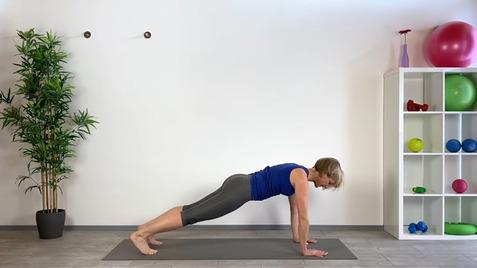 Frau in Sportkleidung in der Plank-Position auf einer Fitnessmatte, neben einer dekorativen Wand mit Fitnessgeräten.