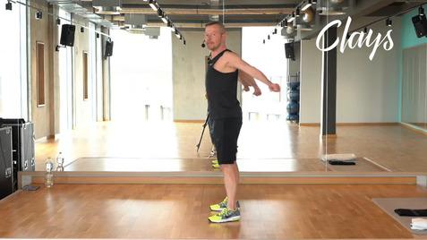 Mann in Sportkleidung führt eine Übung im Fitnessraum vor einem Spiegel aus. Grüne Turnschuhe und Wasserflasche sichtbar.