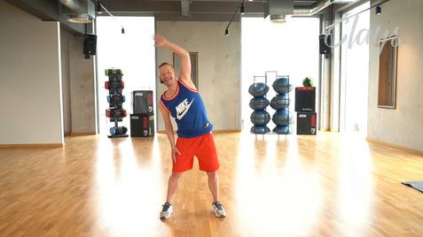 Mann in Sportkleidung führt eine Dehnübung in einem modernen Fitnessraum aus, mit Geräten im Hintergrund.