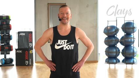 Mann im schwarzen Tanktop mit der Aufschrift „Just Do It“ steht mit Händen auf den Hüften in einem Fitnessraum.