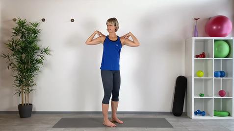 Frau in blauer Sportbekleidung steht auf einer Matte, Arme hinter dem Kopf, mit Fitnessgeräten im Hintergrund.