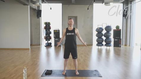 Mann in Sportkleidung steht auf einer Yogamatte in einem modernen Fitnessstudio mit Fitnessgeräten im Hintergrund.