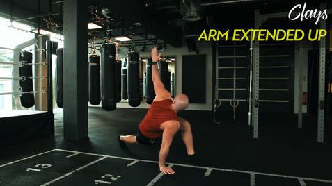 Mann in Sportkleidung führt eine Dehnübung mit einem ausgestreckten Arm in einem Fitnessstudio aus.