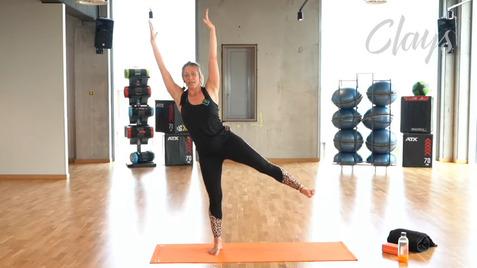 Frau im Fitnessoutfit führt eine Balanceübung auf einer Yogamatte in einem modernen Fitnessstudio aus.