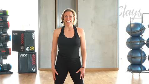 Frau in Sportkleidung steht lächelnd in einem Fitnessstudio, mit Fitnessgeräten im Hintergrund.