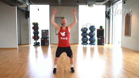 Mann in rotem Muskelshirt mit erhobenen Armen, samstags in einem modernen Fitnessraum mit Sportgeräten.