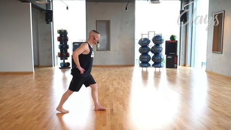 Mann in Sportkleidung führt eine Dehnübung in einem modernen Fitnessstudio mit Holzfußboden aus.