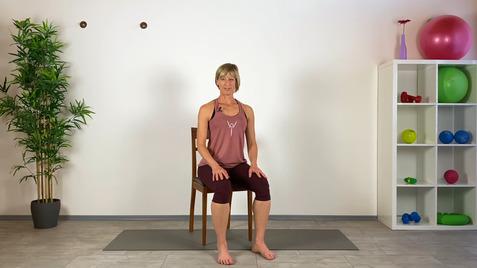 Frau in Sportbekleidung sitzt auf einem Stuhl vor einer Wand, umgeben von Pflanzen und Fitnessgeräten.