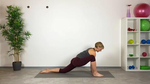 Frau in Yogahaltung auf einer Matte, mit einer Dehnung im linken Bein und einem Pflanzen im Hintergrund.