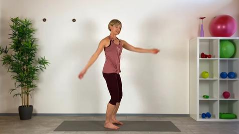 Frau in Fitnesskleidung steht auf einer Matte und führt eine Übung in einem hellen Raum mit Sportgeräten aus.