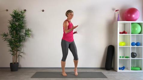 Frau in Sportkleidung steht barfuß auf einer Matte und zeigt eine Übung in einem modernen Fitnessraum.