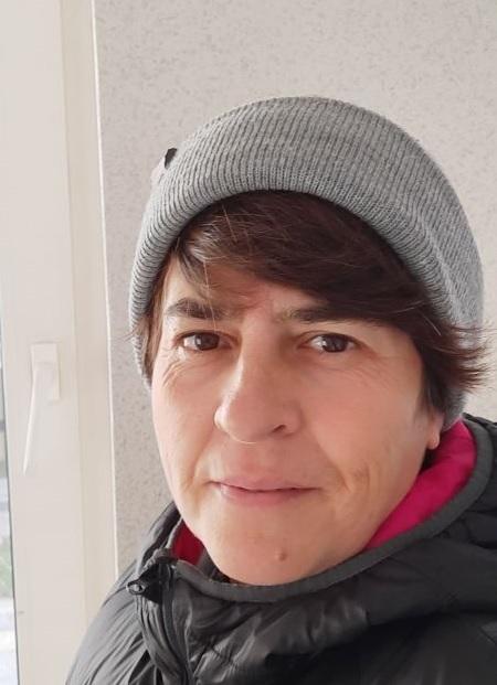 Nahaufnahme einer Person mit grauem Beanie und schwarzer Jacke, vor einem hellen Fenster.