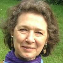 Porträt einer lächelnden Frau mit lockigem Haar, Schmuckohrringen und einem lila Schal, vor grünem Hintergrund.