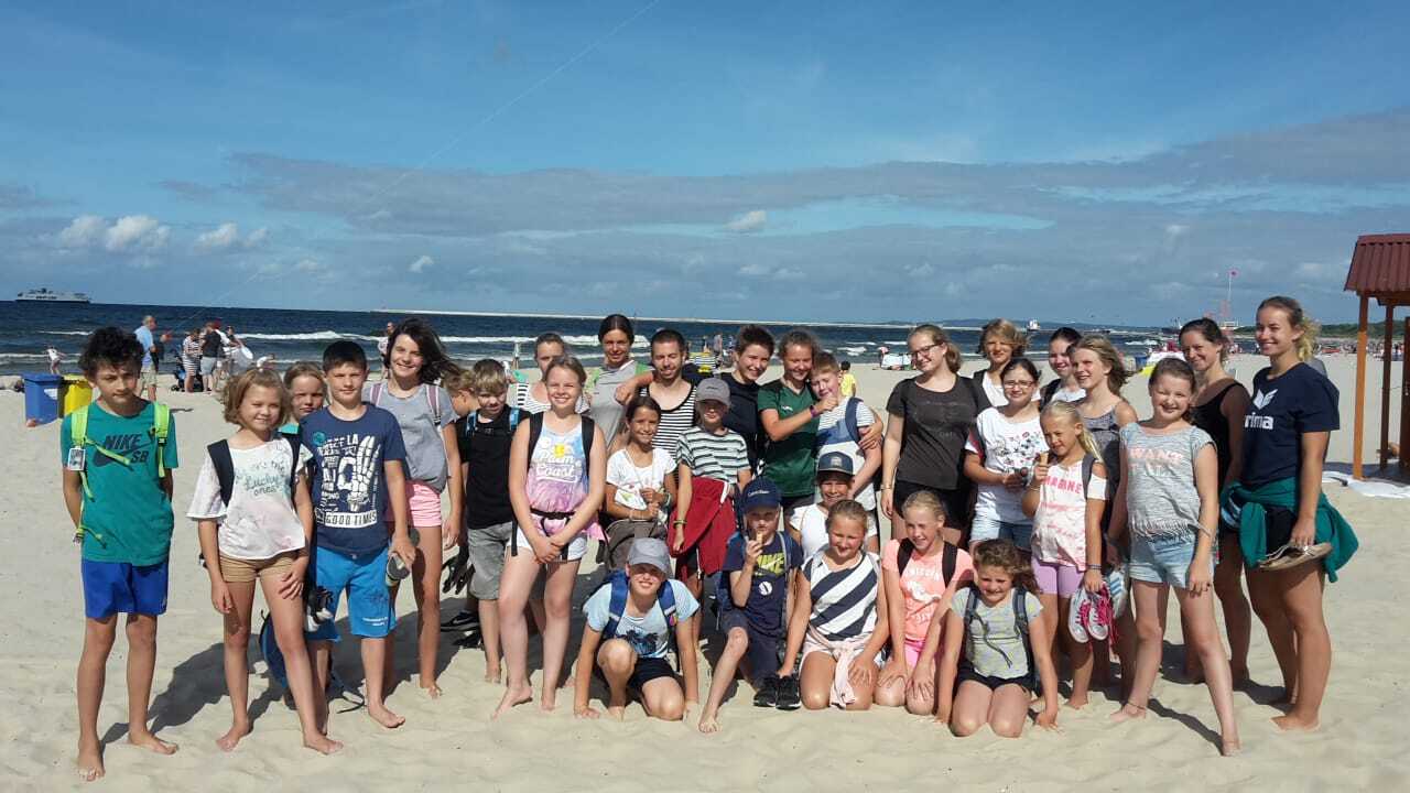Gruppe von Kindern und Jugendlichen am Strand, lächelnd vor einer malerischen Küstenlandschaft.